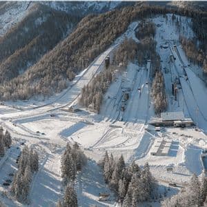 Una vista aerea di un complesso per il salto con gli sci innevato, integrato in un versante montuoso boscoso.