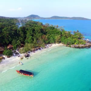 Vista aérea de un barco de cola larga anclado en agua turquesa cristalina junto a una playa de arena blanca bordeada de exuberante bosque.