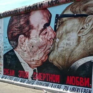 Un primo piano del murale 'Bacio Fraterno' sul Muro di Berlino, che raffigura due uomini che si baciano, coperto di graffiti.