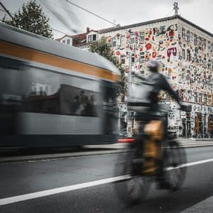 Un ciclista su una strada accanto a un tram in transito, entrambi ripresi con effetto mosso davanti a un edificio coperto di arte colorata.