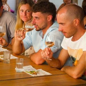 Un viaggio di gruppo WeRoad con persone sedute a un lungo tavolo di legno per una degustazione di vino rosé.