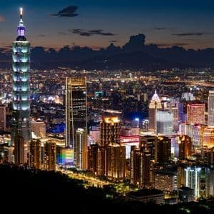 Il grattacielo Taipei 101 e lo skyline circostante sono illuminati di notte, con le montagne visibili in lontananza.