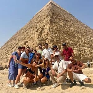 Un groupe WeRoad pose pour une photo devant une grande pyramide en pierre sous un ciel dégagé.