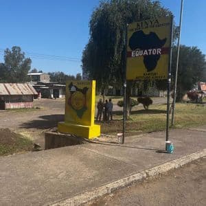 Zwei große gelbe Schilder markieren die Äquatorlinie in Nanyuki, Kenia, an einer Straße unter klarem Himmel.