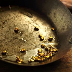 Un primo piano di piccole pepite d'oro che riposano con un po' d'acqua in una padella di metallo scura e usurata.