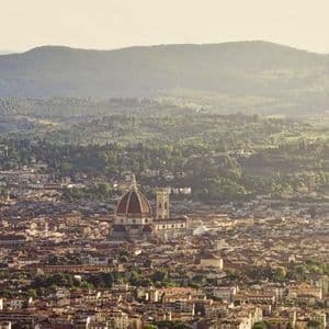 Una vista aerea di una città storica con una grande cupola di cattedrale al suo centro, sullo sfondo di dolci colline verdi.