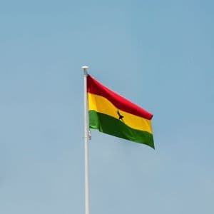La bandiera del Ghana con le sue strisce rosse, gialle e verdi e una stella nera centrale, che sventola su un'asta bianca contro un cielo azzurro e limpido.