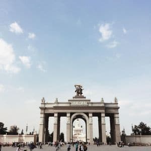 Inquadratura dal basso di un grande arco monumentale in una piazza affollata sotto un cielo luminoso con nuvole leggere.
