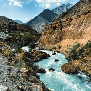 Un fiume azzurro scorre impetuoso attraverso un canyon roccioso di montagna sotto un cielo parzialmente nuvoloso.