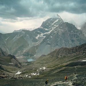 Trekking di gruppo WeRoad lungo un sentiero roccioso in una vasta valle di montagna con un lago sottostante.