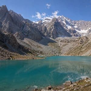 Un lago alpino turchese è circondato da montagne rocciose e innevate, che si riflettono nell'acqua limpida.