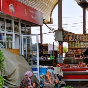 Tre donne velate sono sedute sul selciato di un mercato coperto, parlano e ridono, con ciotole di mele in vendita.