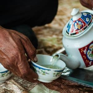 Primo piano delle mani di una persona che versa il tè da una teiera colorata e decorata in una piccola tazza coordinata.