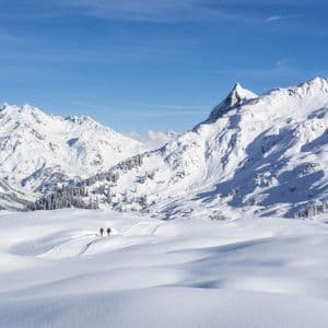 Un viaggio di gruppo WeRoad di due persone che camminano su un sentiero in un vasto paesaggio di montagne innevate sotto un cielo azzurro e limpido.