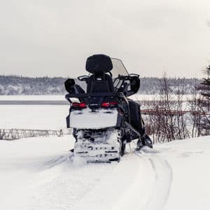 Una motoslitta nera è parcheggiata su un paesaggio innevato, con le sue tracce visibili in primo piano e un lago ghiacciato sullo sfondo.