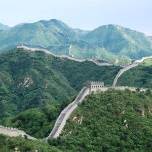 La Grande Muraglia Cinese si snoda attraverso un vasto paesaggio di montagne lussureggianti e verdi sotto un cielo pallido e nuvoloso.