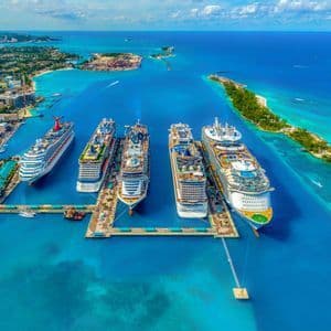 Una vista aerea di diverse grandi navi da crociera attraccate a un molo in un porto turchese, accanto a una città costiera.