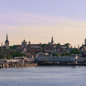 Skyline storico cittadino con numerose guglie di chiese e torri medievali, visto dall'acqua con un porto moderno in primo piano.