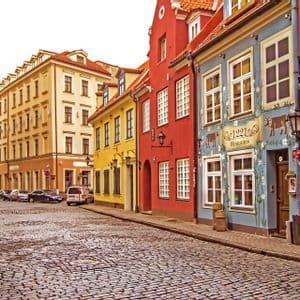 Uno scorcio di una via acciottolata sinuosa, affiancata da edifici colorati e tradizionali, sotto un cielo bianco.