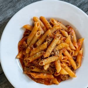 Penne al ragù in una ciotola bianca, guarnite con formaggio e pepe nero.