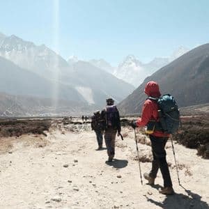 Un viaggio di gruppo WeRoad: escursione su un sentiero polveroso attraverso una valle montana, verso cime innevate distanti, sotto un cielo sereno.