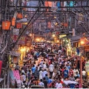 Una grande folla di persone cammina attraverso un mercato di strada stretto e affollato, sotto un fitto e intricato groviglio di cavi elettrici sospesi.