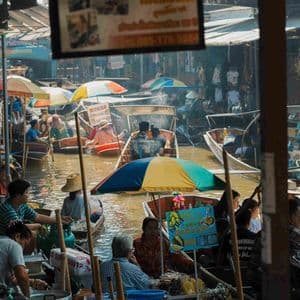 Un vivace mercato galleggiante con molti venditori e turisti su piccole imbarcazioni in un canale affollato.