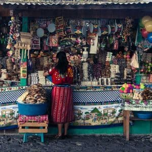 Eine Frau in traditioneller Kleidung steht mit dem Rücken zur Kamera an einem farbenfrohen Marktstand, gefüllt mit Süßigkeiten und Spielzeug.