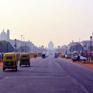Due tuk-tuk gialli e verdi percorrono un'ampia strada verso grandi edifici a cupola in una giornata velata.