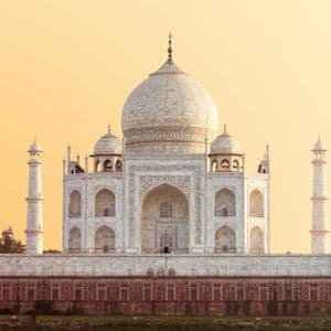Un mausoleo di marmo bianco con una grande cupola centrale e quattro minareti è illuminato da un cielo caldo e dorato all'alba.