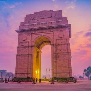 Il monumento India Gate illuminato all'alba, che si staglia su un cielo con nuvole rosa e blu.