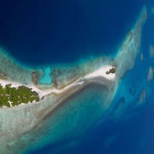 Veduta aerea di un'isola tropicale, con il suo banco di sabbia bianca e la barriera corallina che contrastano con il mare turchese e blu profondo.