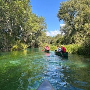 Un viaje en grupo de WeRoad navegando en canoa por un río verde y cristalino rodeado de frondosos árboles en un día soleado.