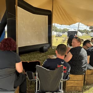 A WeRoad group trip sits under a large tent, watching an inflatable movie screen during an outdoor event.