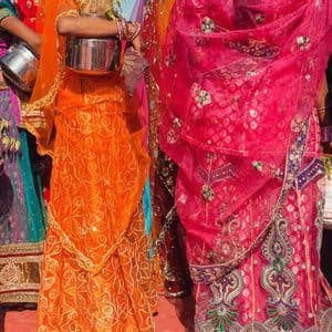 Un grupo de mujeres de pie, muy unidas, luciendo vibrantes y coloridos saris indios tradicionales y sosteniendo pequeñas vasijas.