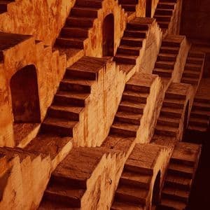 Una rete intricata di scalinate in pietra intrecciate scende con un motivo geometrico all'interno di un antico pozzo a gradini.