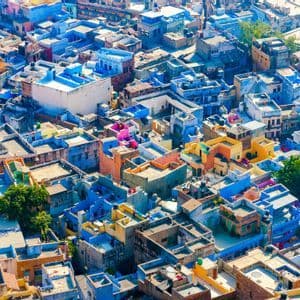 Una vista aerea di una città densa, con molti edifici dai tetti piatti dipinti in tonalità di blu, giallo e rosa.