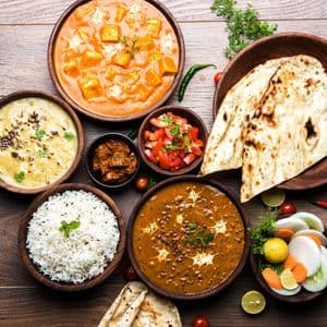 Une vue de dessus d'un repas indien traditionnel, avec divers currys, du riz et du pain naan servis dans des bols sur une surface en bois.