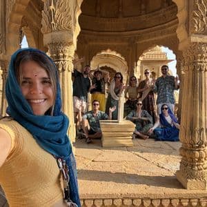 Una mujer con un pañuelo azul se toma una selfie con su viaje en grupo de WeRoad dentro de un pabellón de arenisca ornamentado.