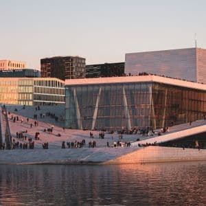 People walking and gathering on the sloping marble roof of a modern waterfront opera building at sunset.