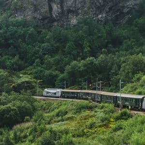 A passenger train traveling along railway tracks on a steep, lush green forested mountain slope.
