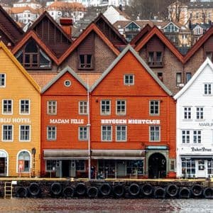 Colorful wooden gabled waterfront buildings stand in a row along a stone harbor quay lined with tires.