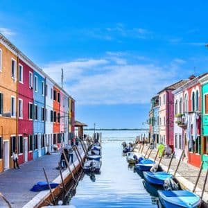Brightly colored houses line a narrow canal filled with docked boats under a clear blue sky.