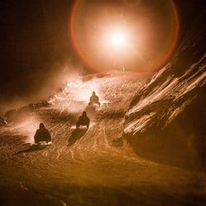 Un viaggio di gruppo WeRoad in slitta lungo un pendio innevato di notte, illuminato da una brillante luce dall'alto.