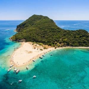 Vista aerea di un'isola alberata con una lingua di sabbia dove le barche sono ormeggiate e le persone si godono l'acqua turchese.