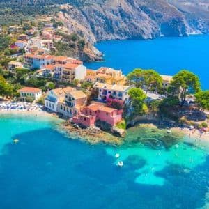 Vista aerea di un pittoresco villaggio costiero arroccato su una scogliera, che domina una baia turchese e luminosa con spiaggia e bagnanti.