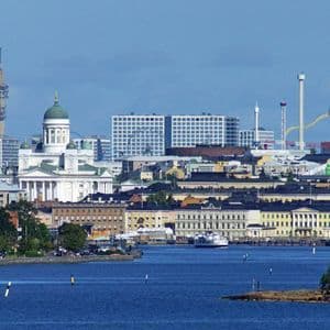 Un paysage urbain vu de la mer, avec une cathédrale blanche au dôme vert, un ferry sur l'eau et un parc d'attractions en arrière-plan.