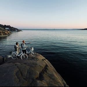 Deux personnes d'un voyage en groupe WeRoad avec leurs vélos sur une falaise rocheuse, admirant la mer au coucher du soleil.
