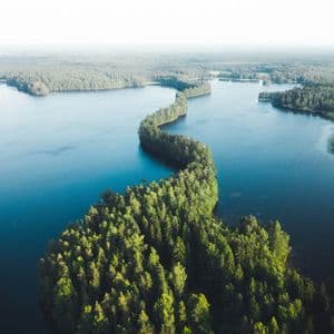 Une vue aérienne d'une longue péninsule sinueuse couverte d'arbres verts denses, serpentant à travers un lac bleu calme sous un ciel brumeux.
