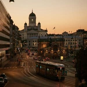 Un tramway circule sur les rails d'une rue urbaine au coucher du soleil, avec une grande cathédrale à dôme visible au loin.